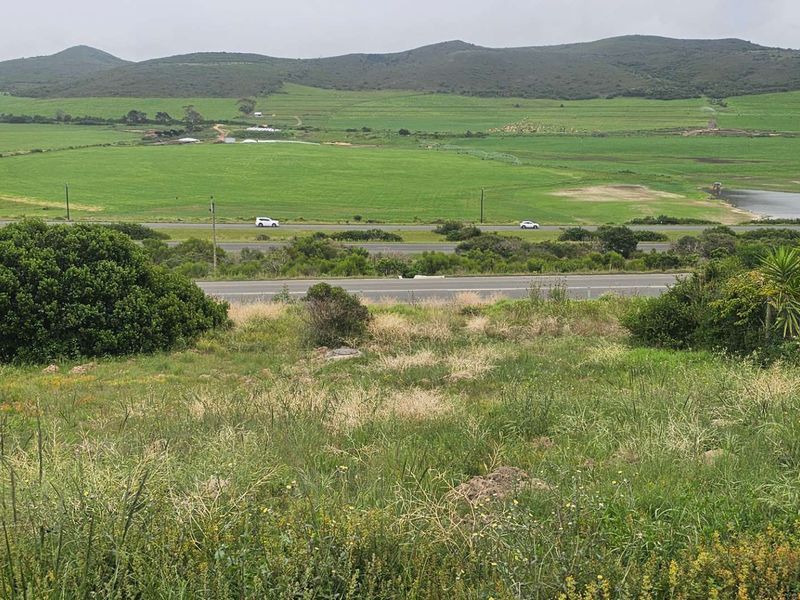 A scenic view overlooking open green fields, rolling hills, and a nearby road, showcasing the natural landscape surrounding the vacant residential land.