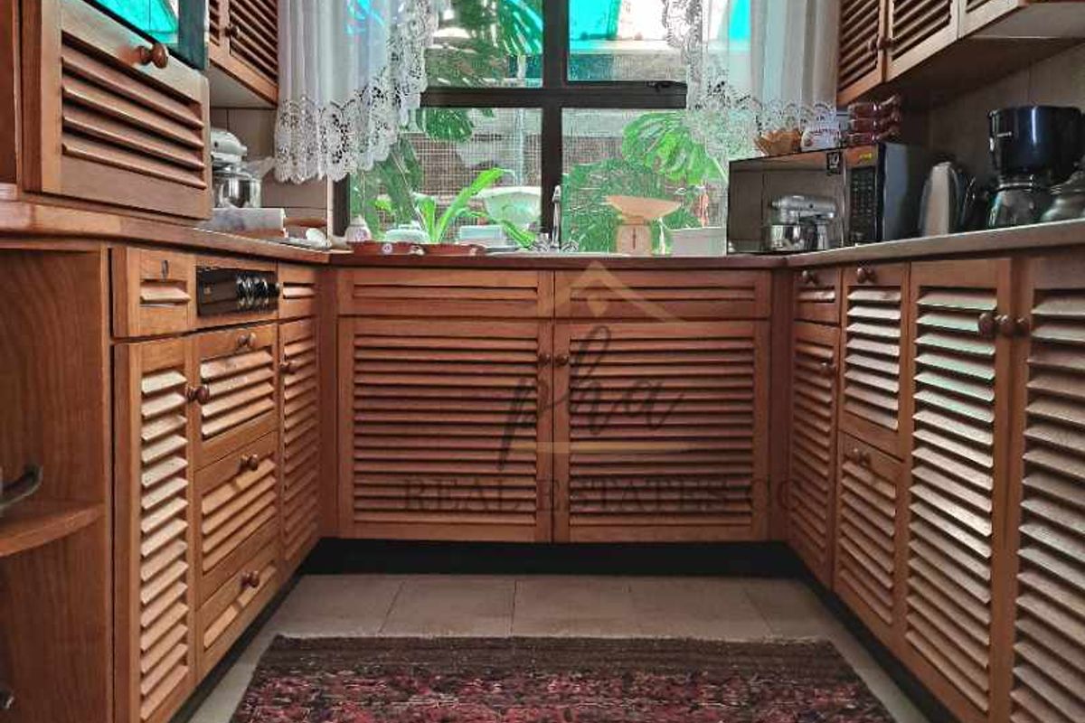 A U-shaped kitchen featuring traditional timber louvered cabinetry, integrated oven, and a large window providing natural light and garden views.