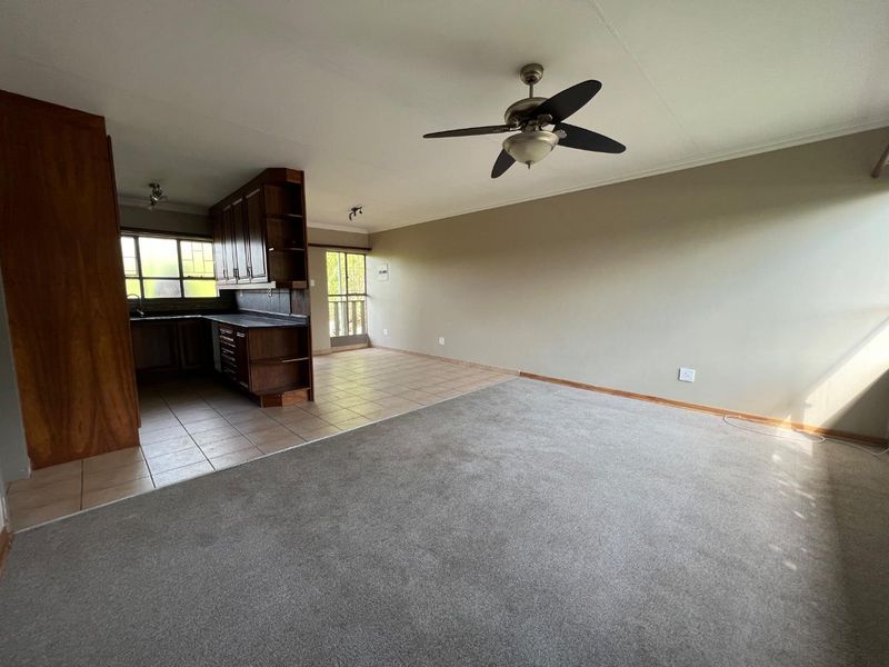 Spacious open-plan living area featuring a kitchen with wooden cabinetry, tiled and carpeted flooring, and a ceiling fan.