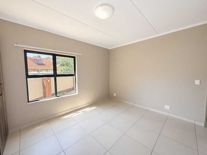 A bright, empty bedroom featuring neutral wall tones, tiled flooring, and an aluminium-framed window, providing a clean canvas for personalization.