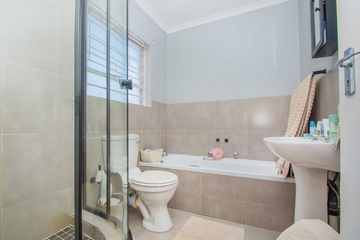 A functional bathroom featuring a built-in bathtub, pedestal sink, toilet, and a separate glass-enclosed shower with neutral wall tiling.