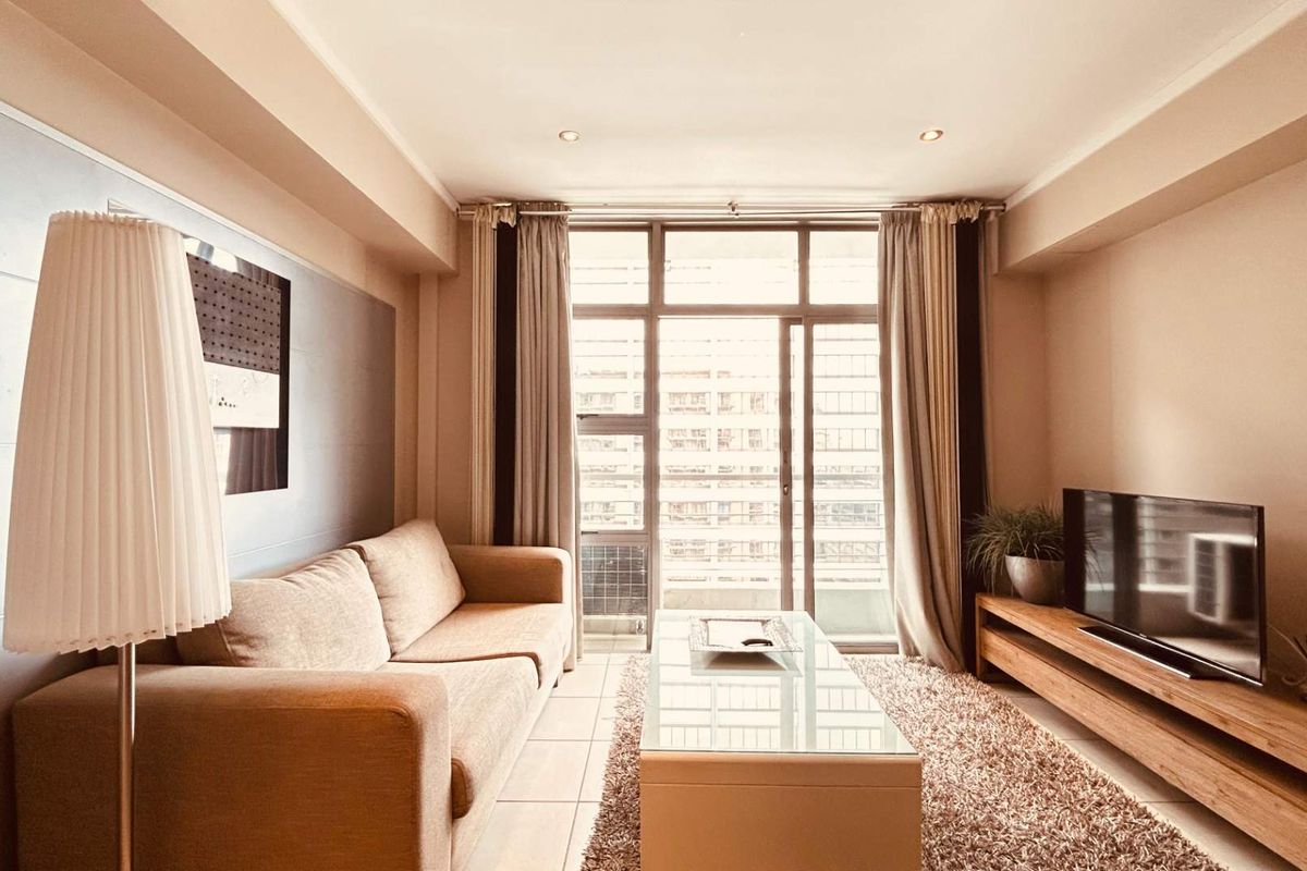 A well-maintained living room featuring tiled flooring, recessed downlighting, and a large sliding glass door providing access to the balcony.