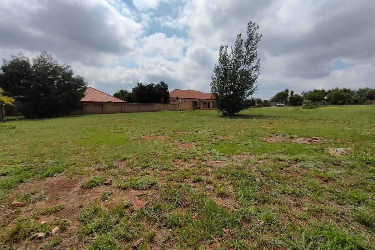 A wide-angle view of a vacant residential plot featuring established grass, mature trees, and perimeter boundary walls.