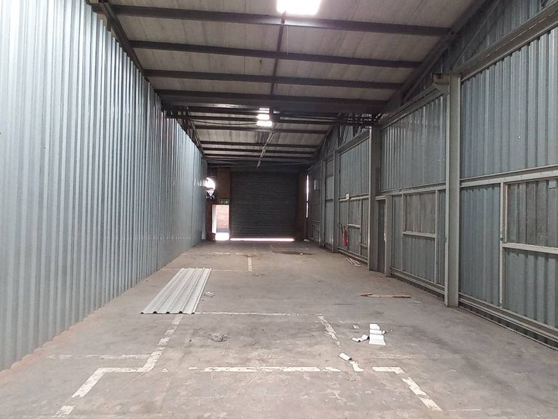 Spacious industrial utility area featuring corrugated metal walls, exposed steel roof trusses, concrete flooring, and a large roller shutter door for easy access.