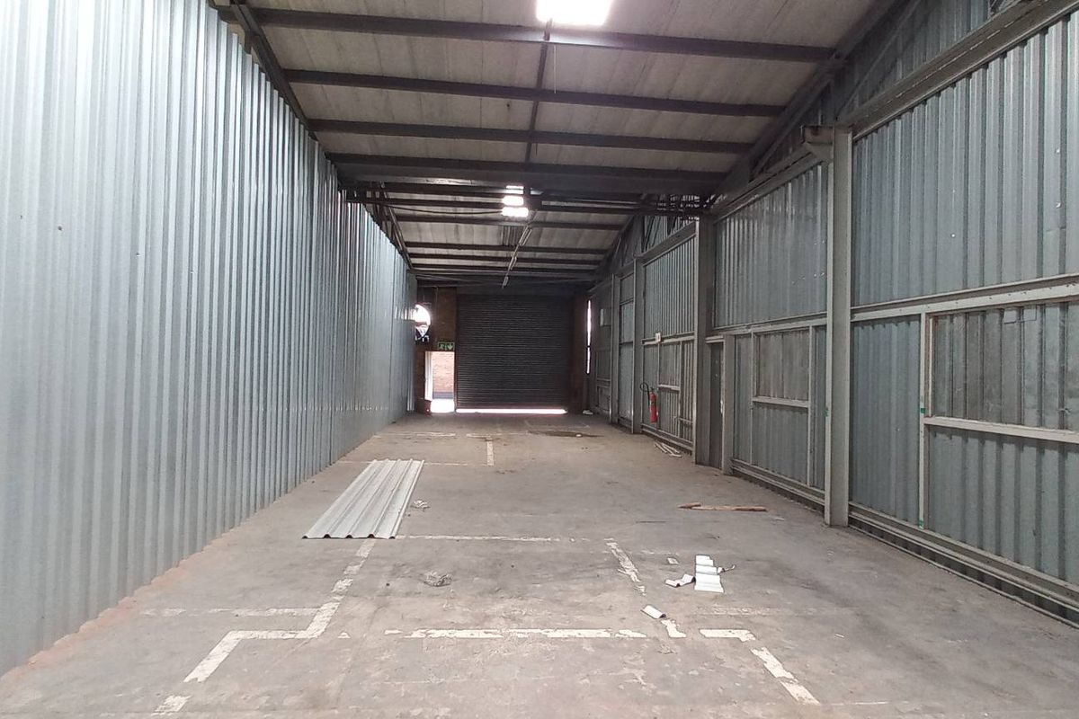 Spacious industrial utility area featuring corrugated metal walls, exposed steel roof trusses, concrete flooring, and a large roller shutter door for easy access.