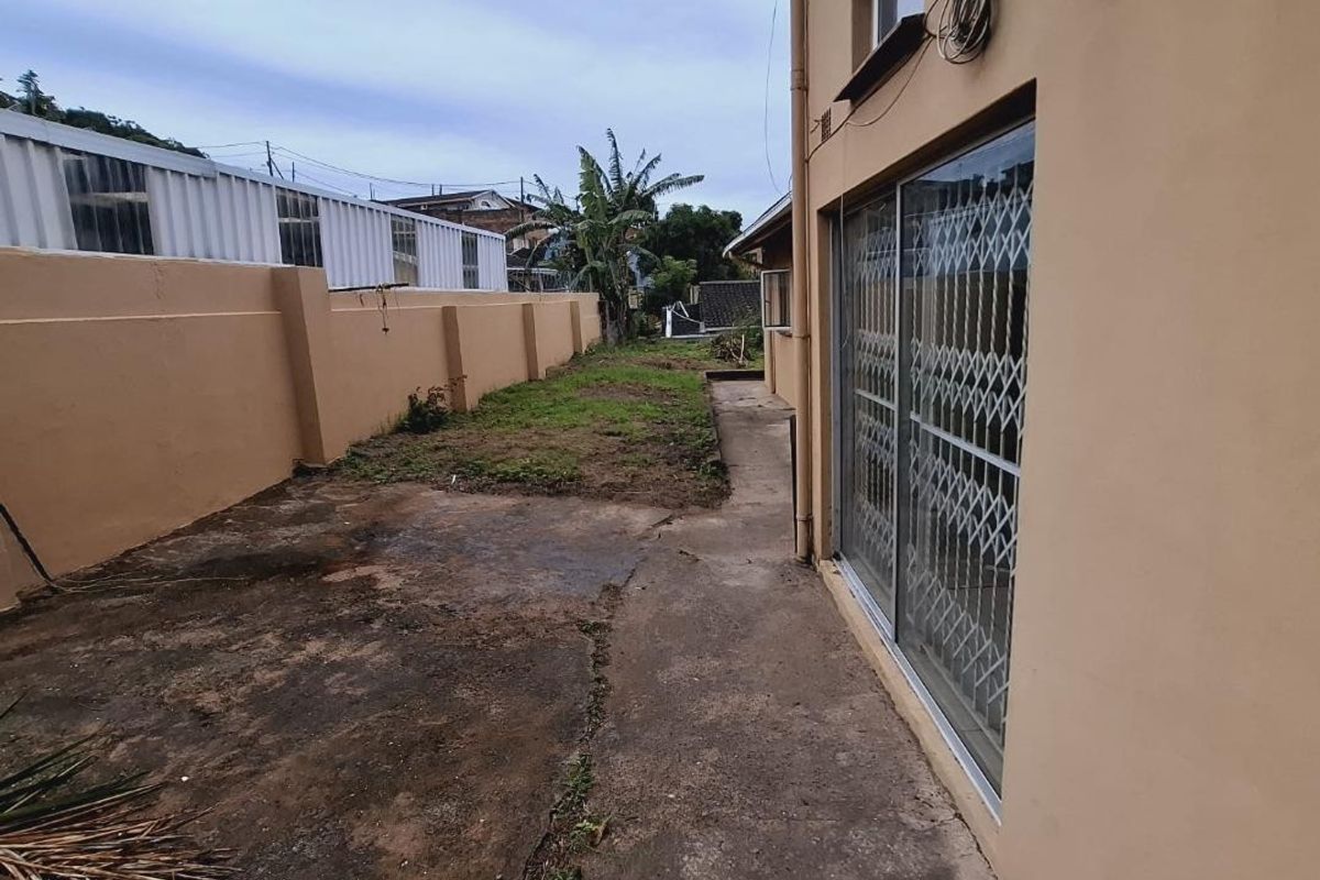 Rear exterior view showing a concrete pathway, boundary wall, and sliding glass door with security gate access.