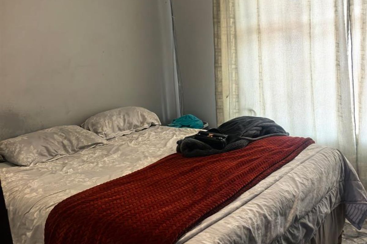 A bedroom featuring tiled flooring, decorative ceiling cornicing, and a large window with curtains.