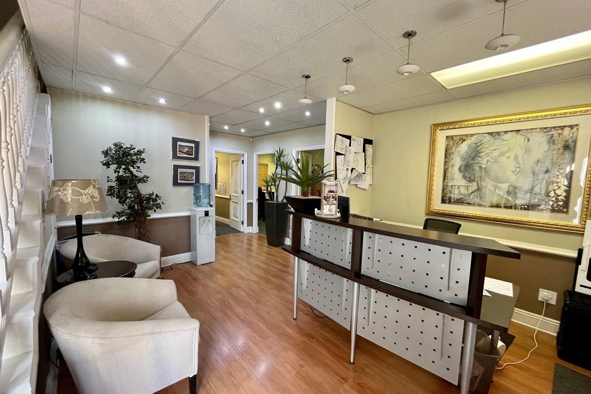 A professional reception area featuring laminate flooring, a built-in reception desk, drop ceiling with recessed lighting, and access to multiple internal office spaces.