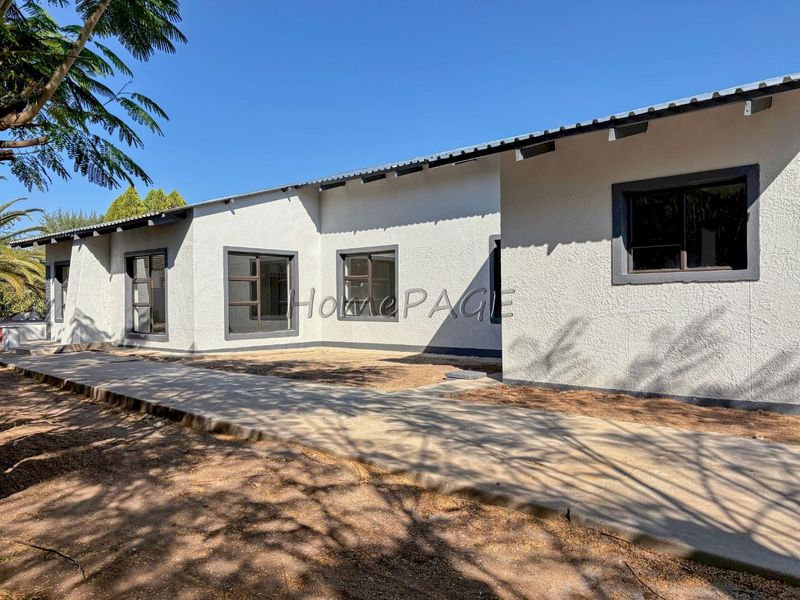 Rear view of the house featuring a concrete walkway, textured exterior walls, and aluminium window frames under a corrugated metal roof.
