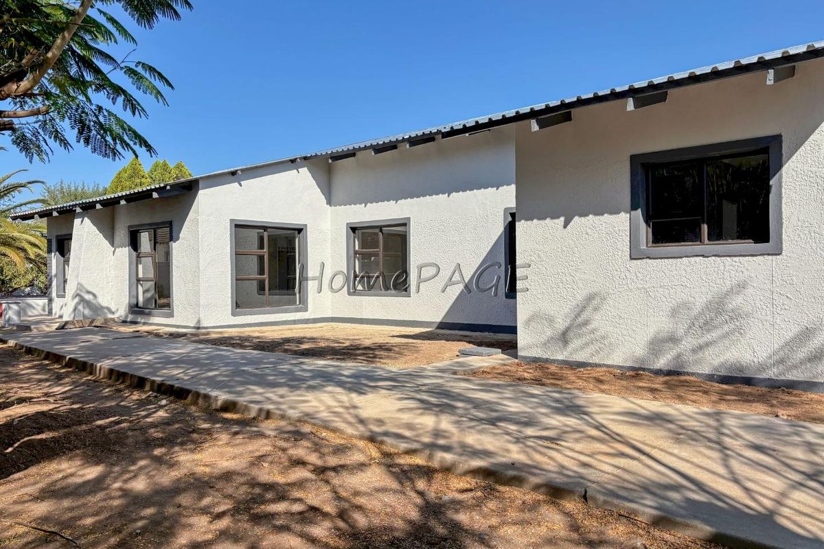 Rear view of the house featuring a concrete walkway, textured exterior walls, and aluminium window frames under a corrugated metal roof.