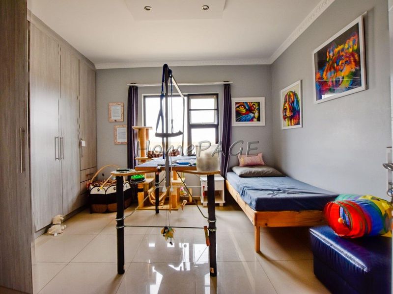 A well-maintained bedroom featuring neutral tiled flooring, built-in cupboards, and recessed ceiling lighting, offering a functional and clean living space.