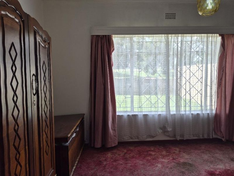 A bedroom featuring a large window with security bars, fitted curtain rails, and wall-to-wall carpeting.