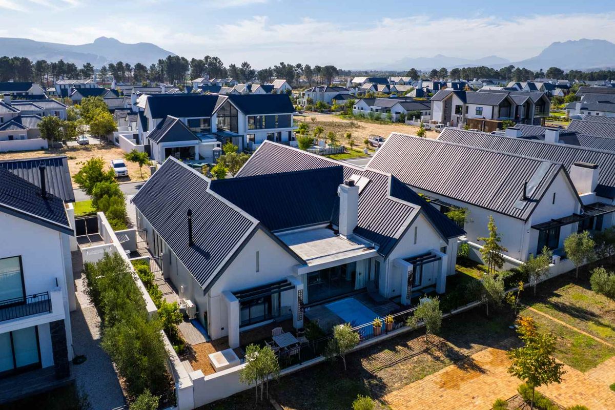 Aerial view of a modern residential property featuring a dark metal roof, white exterior walls, and a private rear patio area within a housing estate.