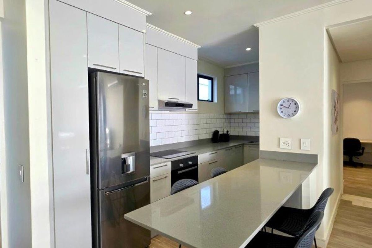 Modern kitchen featuring sleek white cabinetry, stone countertops, a breakfast bar, subway tile backsplash, and integrated appliances in a bright, open-plan layout.