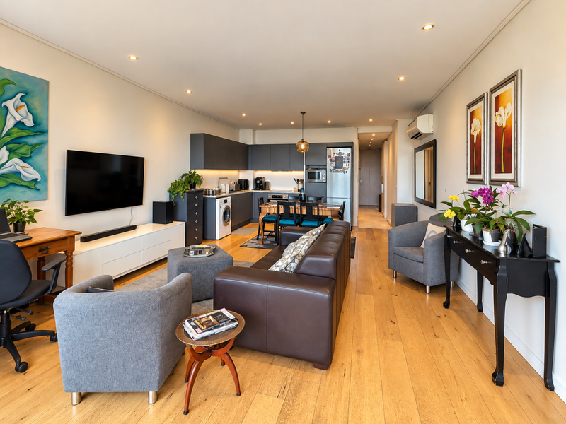 A spacious open-plan living and kitchen area featuring modern cabinetry, integrated appliances, hardwood flooring, and recessed lighting, creating a bright and functional living space.