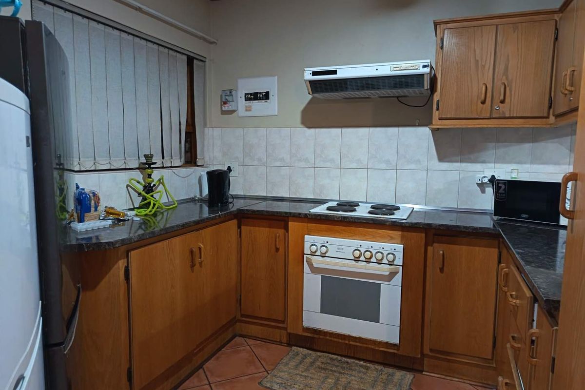 A functional kitchen featuring wooden cabinetry, granite-look countertops, a built-in oven with electric hob, and an extractor fan.