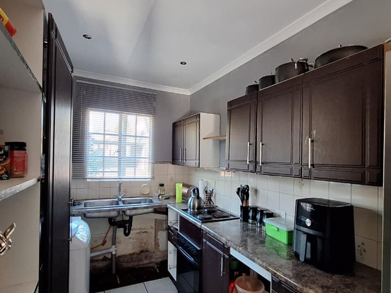 A compact kitchen featuring dark cabinetry, a double basin sink, and built-in oven and hob, currently showing signs of wear and maintenance requirements.