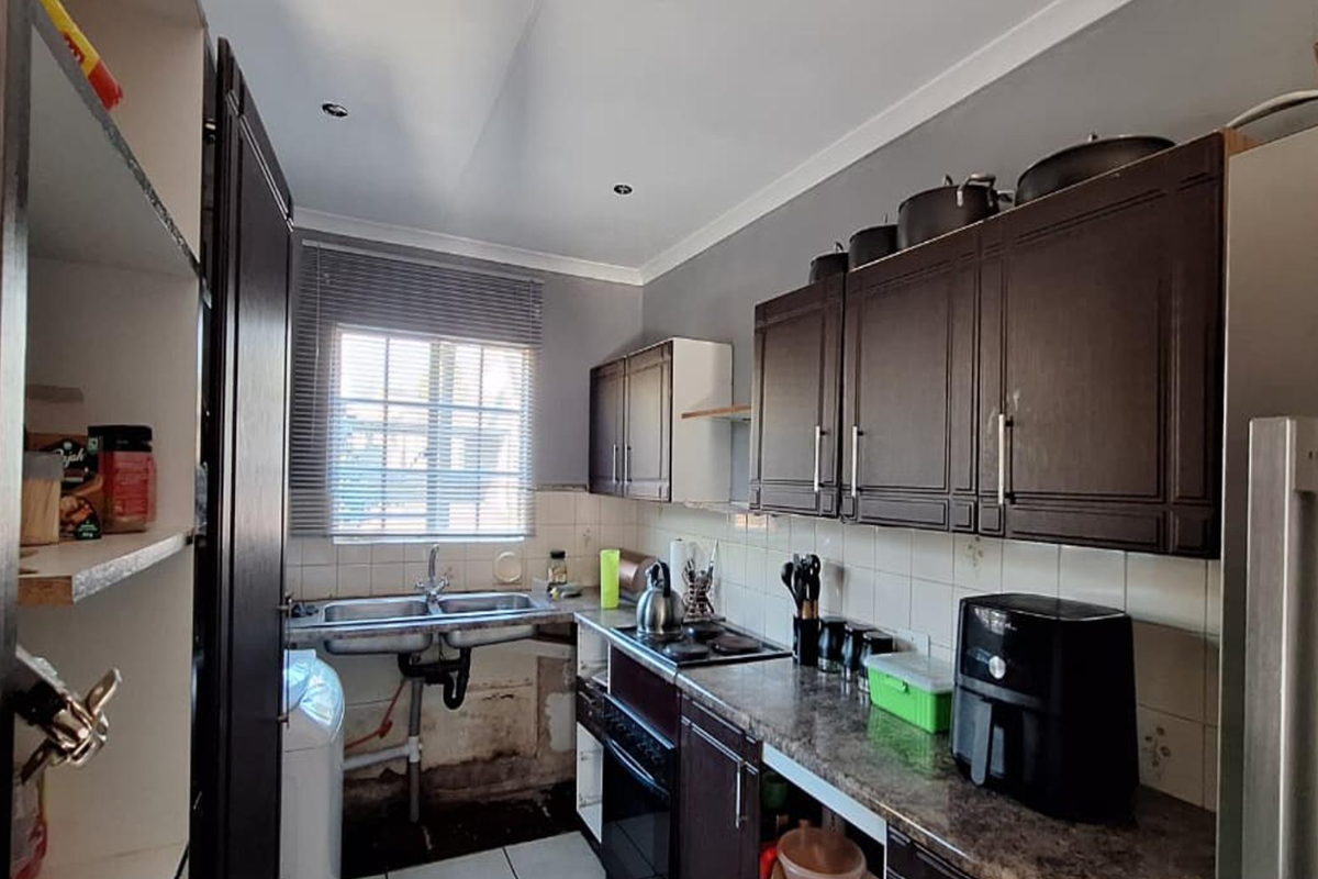 A compact kitchen featuring dark cabinetry, a double basin sink, and built-in oven and hob, currently showing signs of wear and maintenance requirements.