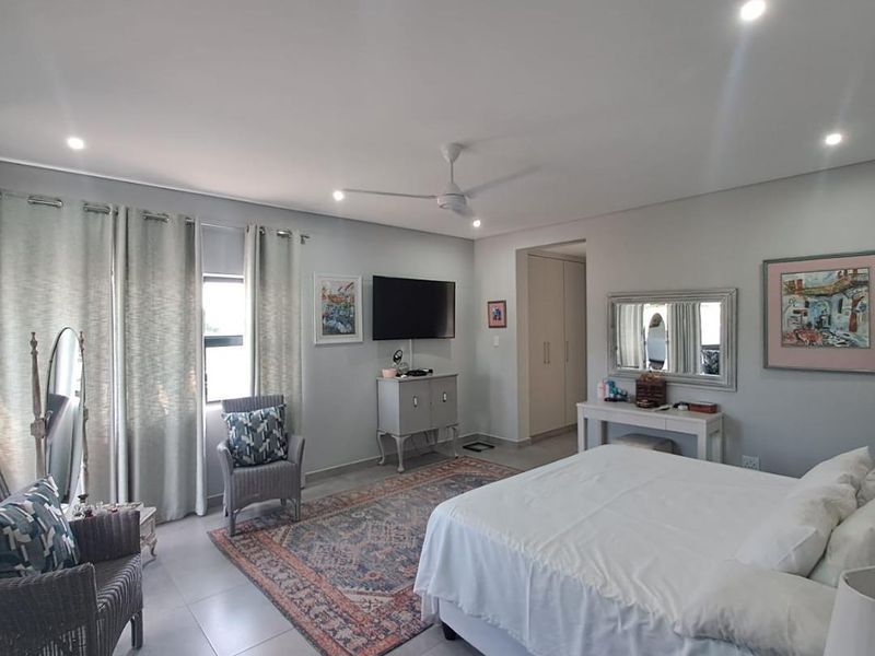 Spacious bedroom featuring neutral tiled flooring, recessed downlighting, a ceiling fan, and built-in storage cupboards.