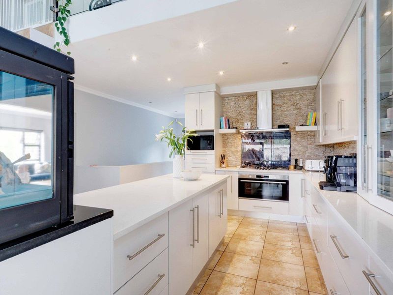 Modern kitchen featuring a central island, stone countertops, built-in appliances, and a decorative stone feature wall with recessed lighting.