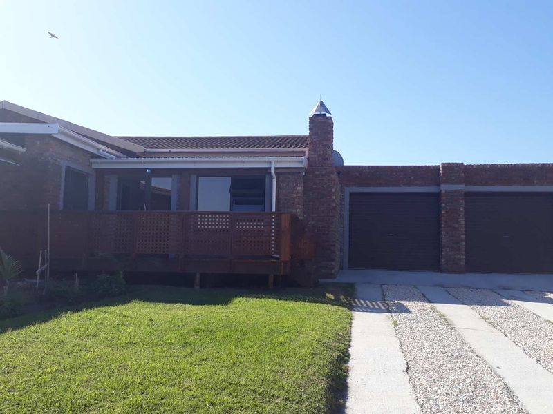 Front view of a brick house featuring a double garage, gravel driveway, and an elevated wooden deck area.