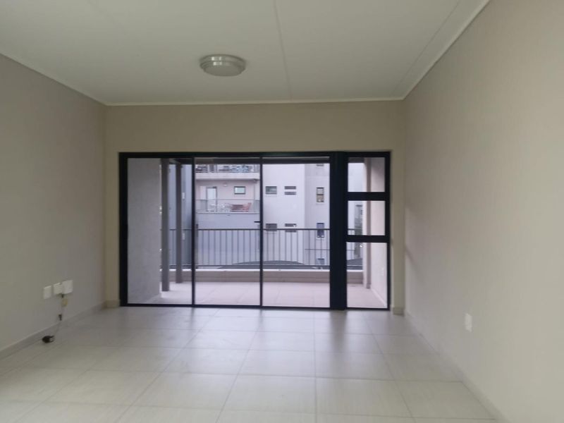 A bright, empty living room featuring neutral tiled flooring and a large sliding glass door providing access to an outdoor balcony area.
