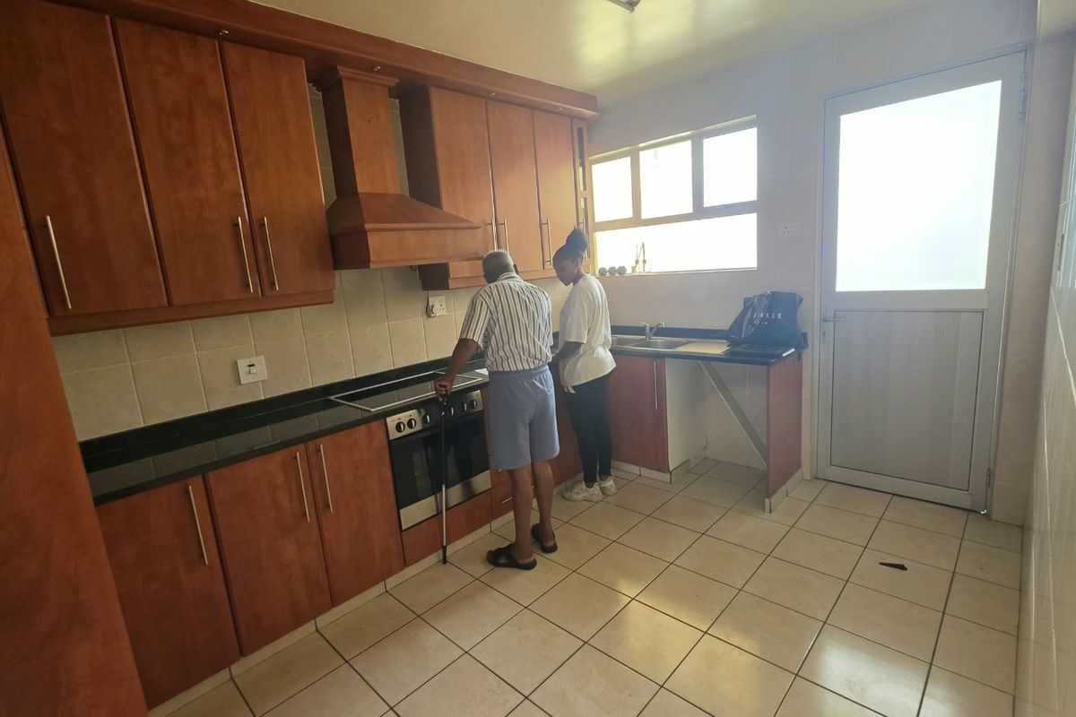 A functional kitchen featuring wooden cabinetry, built-in oven with hob, extractor fan, tiled backsplash, and direct access to an exterior door.