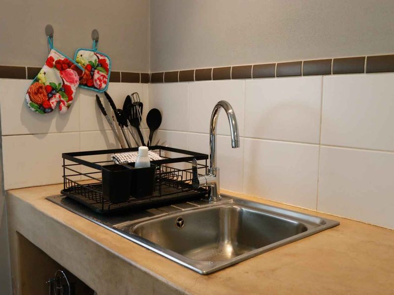 A functional kitchen sink area featuring a stainless steel basin, modern gooseneck faucet, and a tiled backsplash with a durable concrete countertop.