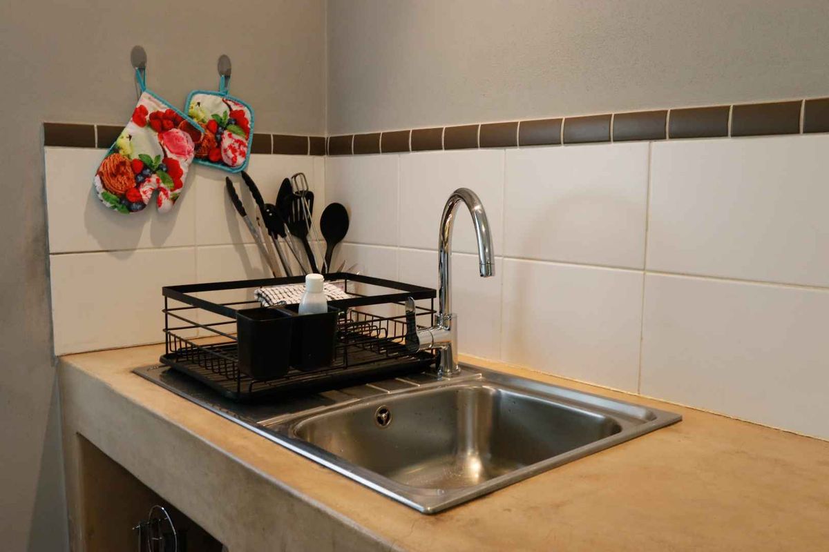 A functional kitchen sink area featuring a stainless steel basin, modern gooseneck faucet, and a tiled backsplash with a durable concrete countertop.