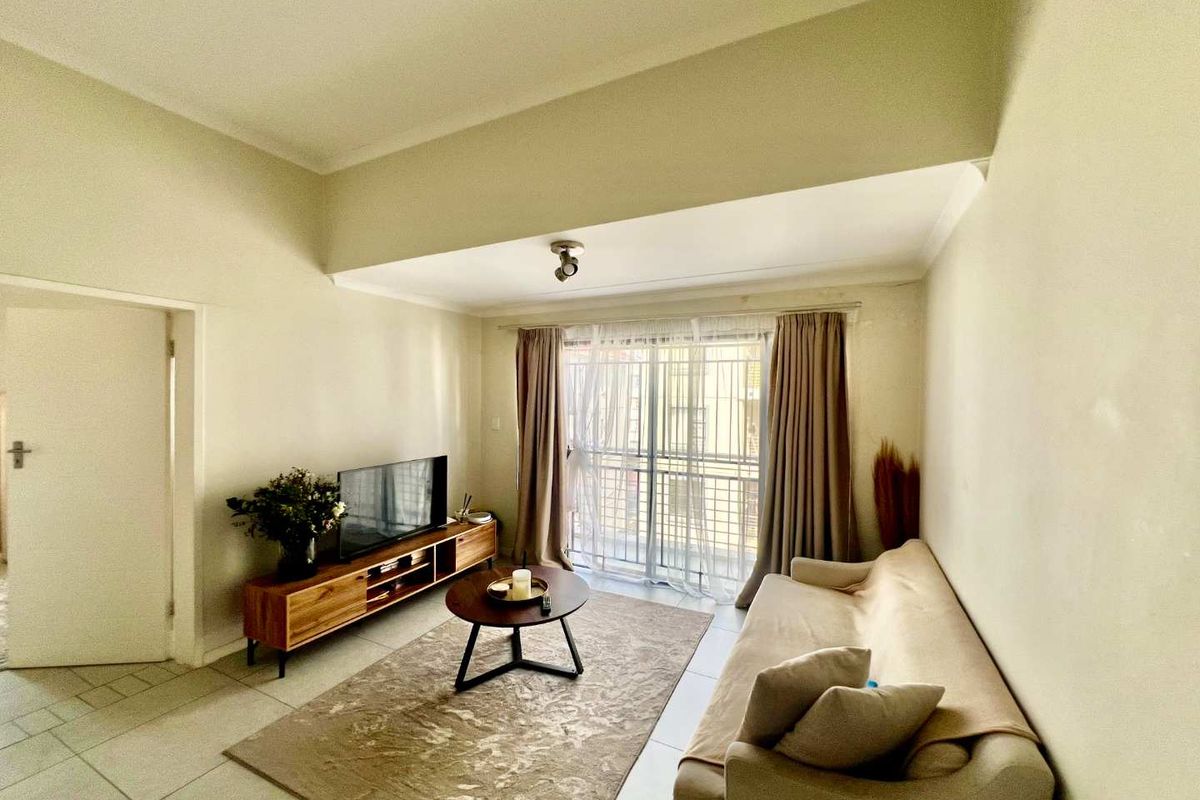 A bright living room featuring tiled flooring, a bulkhead ceiling detail, and sliding glass doors leading to a balcony with security bars.