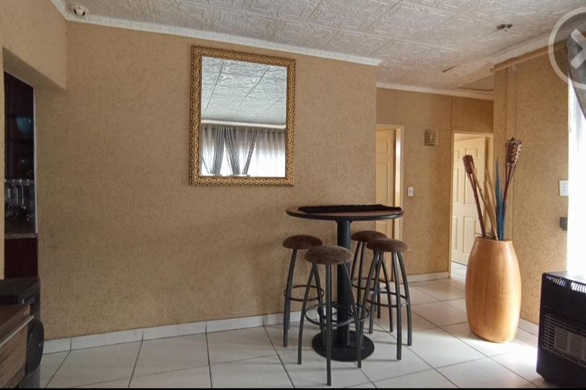 A living area featuring tiled flooring, textured walls, and a decorative ceiling, providing a functional space with access to adjacent rooms.