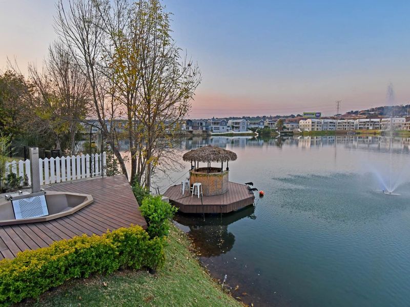 Scenic waterfront view featuring a timber deck with a built-in spa, a floating gazebo on the lake, and a landscaped garden area.