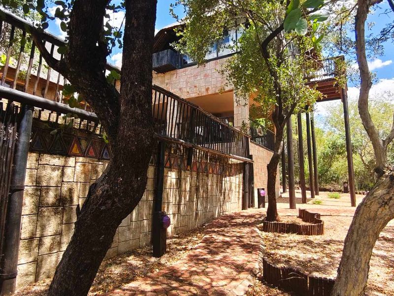 Rear view of a multi-level property featuring stone cladding, a raised wooden deck with metal railings, and a thatched roof set in a natural landscape.