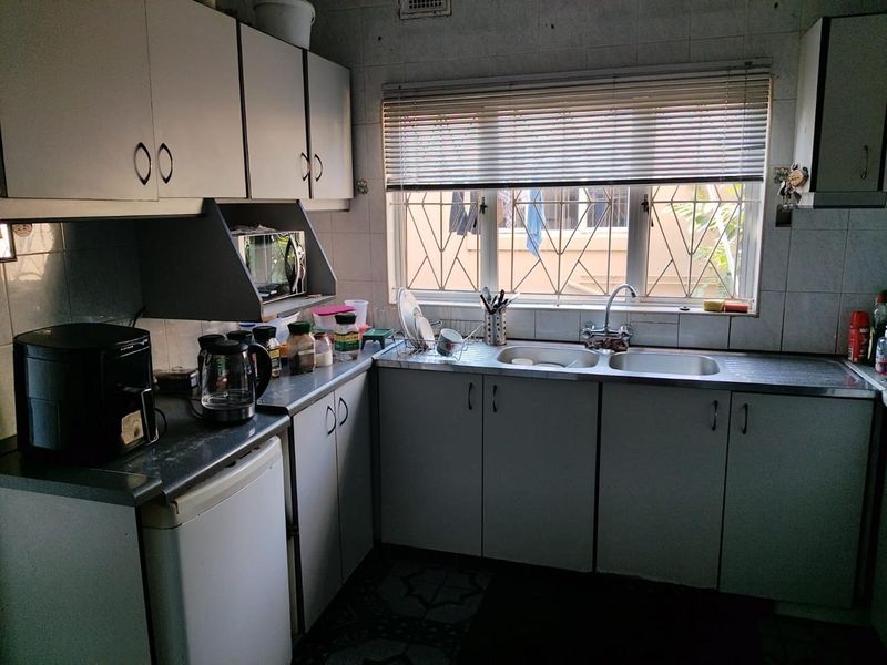 A functional kitchen featuring laminate cabinetry, a double bowl stainless steel sink, and tiled splashbacks, offering potential for a modern renovation.