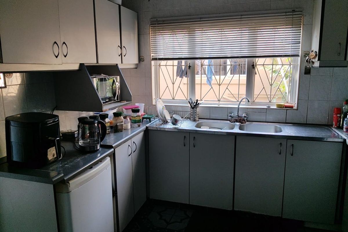 A functional kitchen featuring laminate cabinetry, a double bowl stainless steel sink, and tiled splashbacks, offering potential for a modern renovation.