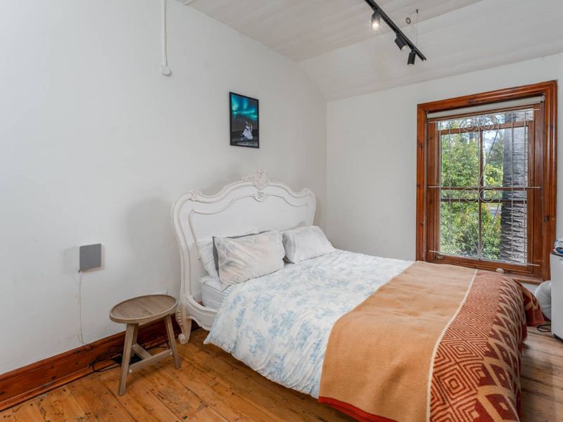 A bedroom featuring timber flooring, track lighting, and a window with security bars, showing signs of wear on the timber finishes.