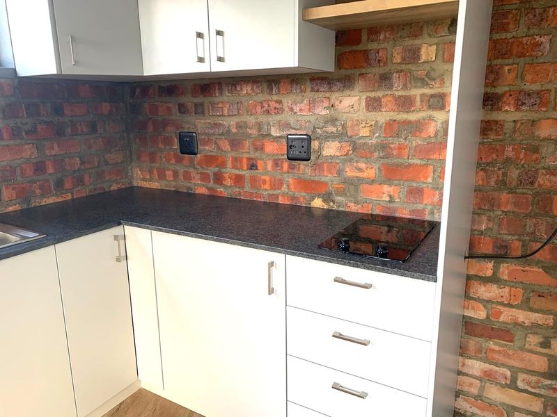 Modern kitchen area featuring white cabinetry, dark laminate countertops, a built-in electric hob, and an exposed brick feature wall.