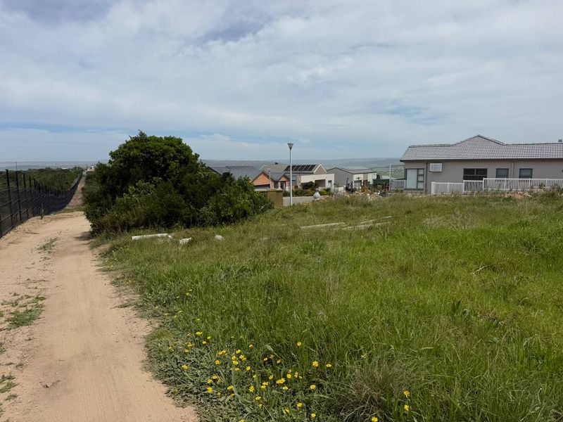 A view of a vacant residential plot featuring natural grass cover, perimeter fencing, and surrounding established residential properties.