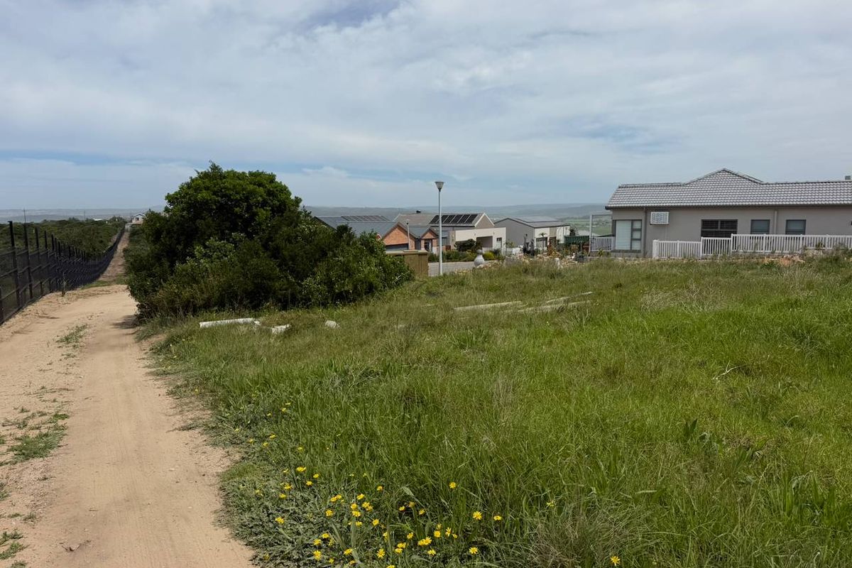 A view of a vacant residential plot featuring natural grass cover, perimeter fencing, and surrounding established residential properties.