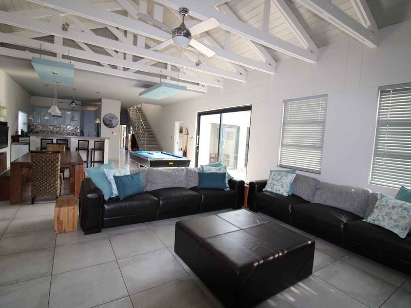 Spacious open-plan living area featuring exposed vaulted ceiling beams, tiled flooring, and seamless flow to the kitchen and staircase.