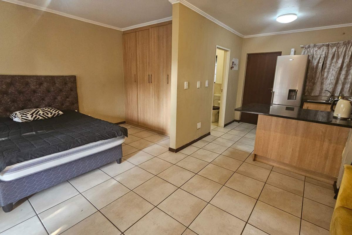 Open-plan studio apartment featuring a combined bedroom and kitchen area with built-in cupboards, granite countertops, and tiled flooring throughout.