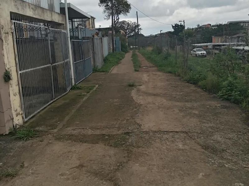 A view of the exterior access path and driveway area showing weathered concrete surfaces and perimeter security fencing.