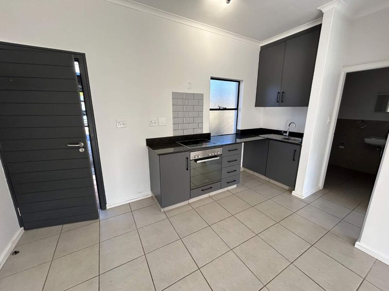 Modern kitchen featuring dark grey cabinetry, granite countertops, built-in oven and hob, subway tile backsplash, and neutral floor tiles.