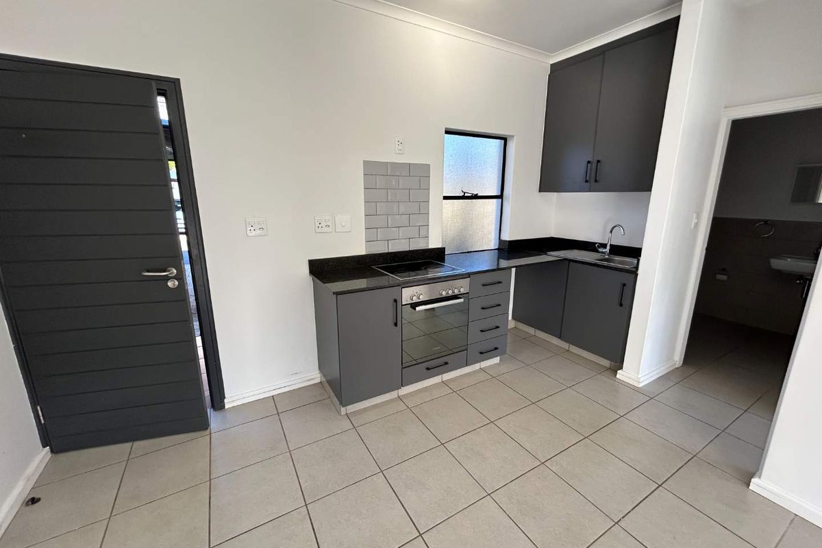 Modern kitchen featuring dark grey cabinetry, granite countertops, built-in oven and hob, subway tile backsplash, and neutral floor tiles.