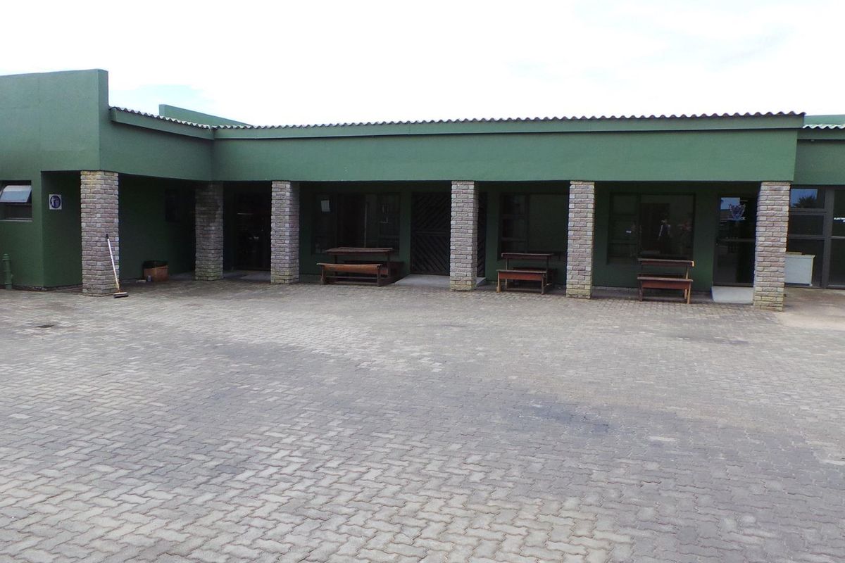 Exterior view of a commercial building featuring a paved courtyard, covered walkway with brick pillars, and multiple access points.