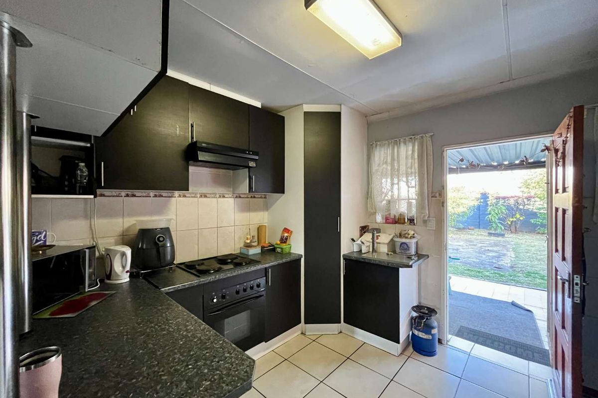 A functional kitchen featuring dark cabinetry, laminate countertops, built-in oven and hob, tiled flooring, and direct access to the rear garden area.