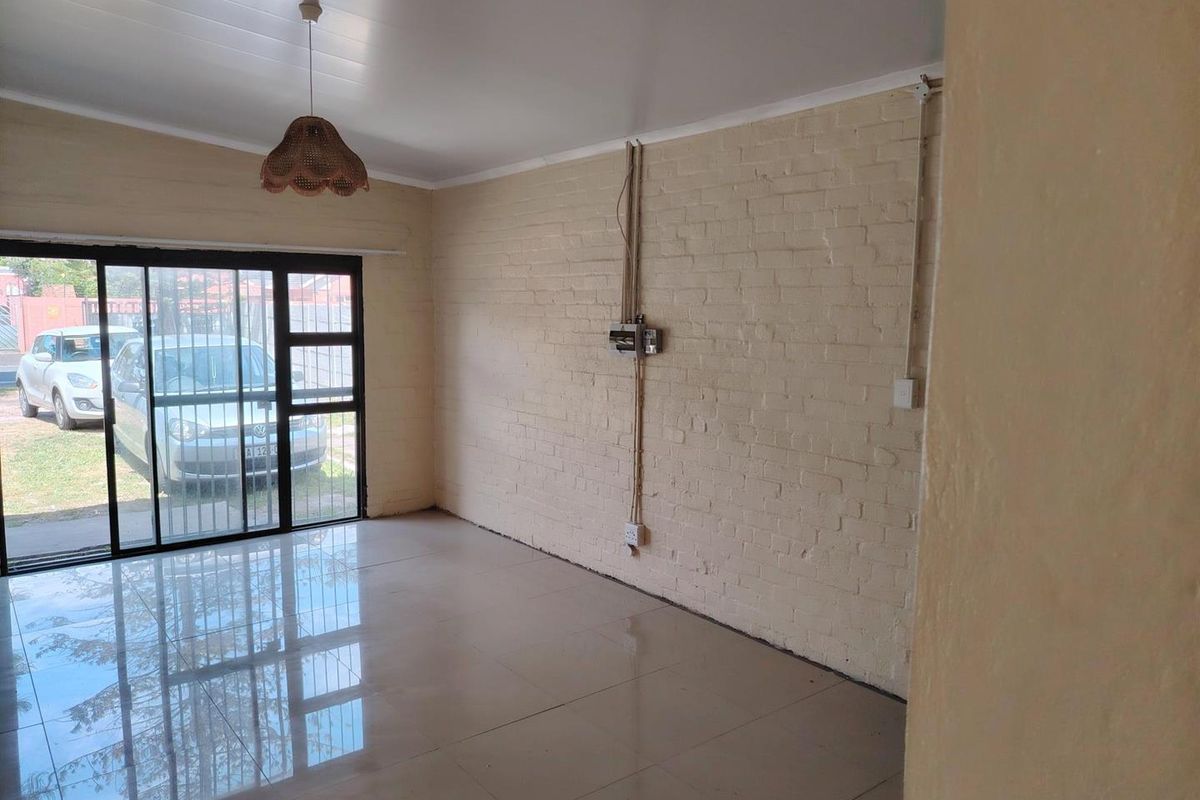 An empty living room featuring ceramic tile flooring, an exposed brick wall, and a sliding glass door providing access to the exterior.