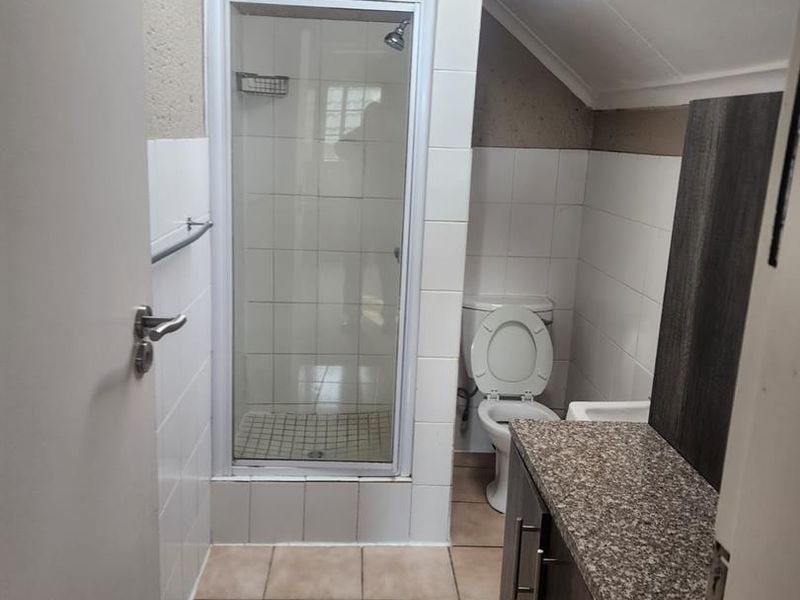 Compact bathroom featuring a shower enclosure, toilet, vanity with granite countertop, and a skylight providing natural light.