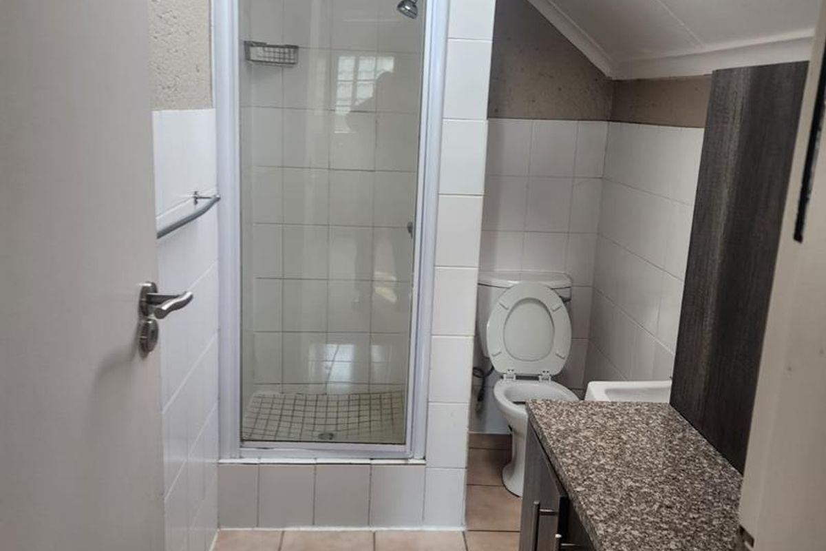 Compact bathroom featuring a shower enclosure, toilet, vanity with granite countertop, and a skylight providing natural light.
