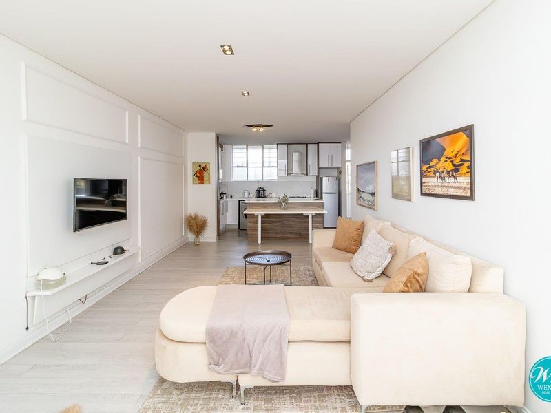 Modern open-plan living area featuring light laminate flooring, decorative wall paneling, and a functional kitchen with a central island and integrated cabinetry.